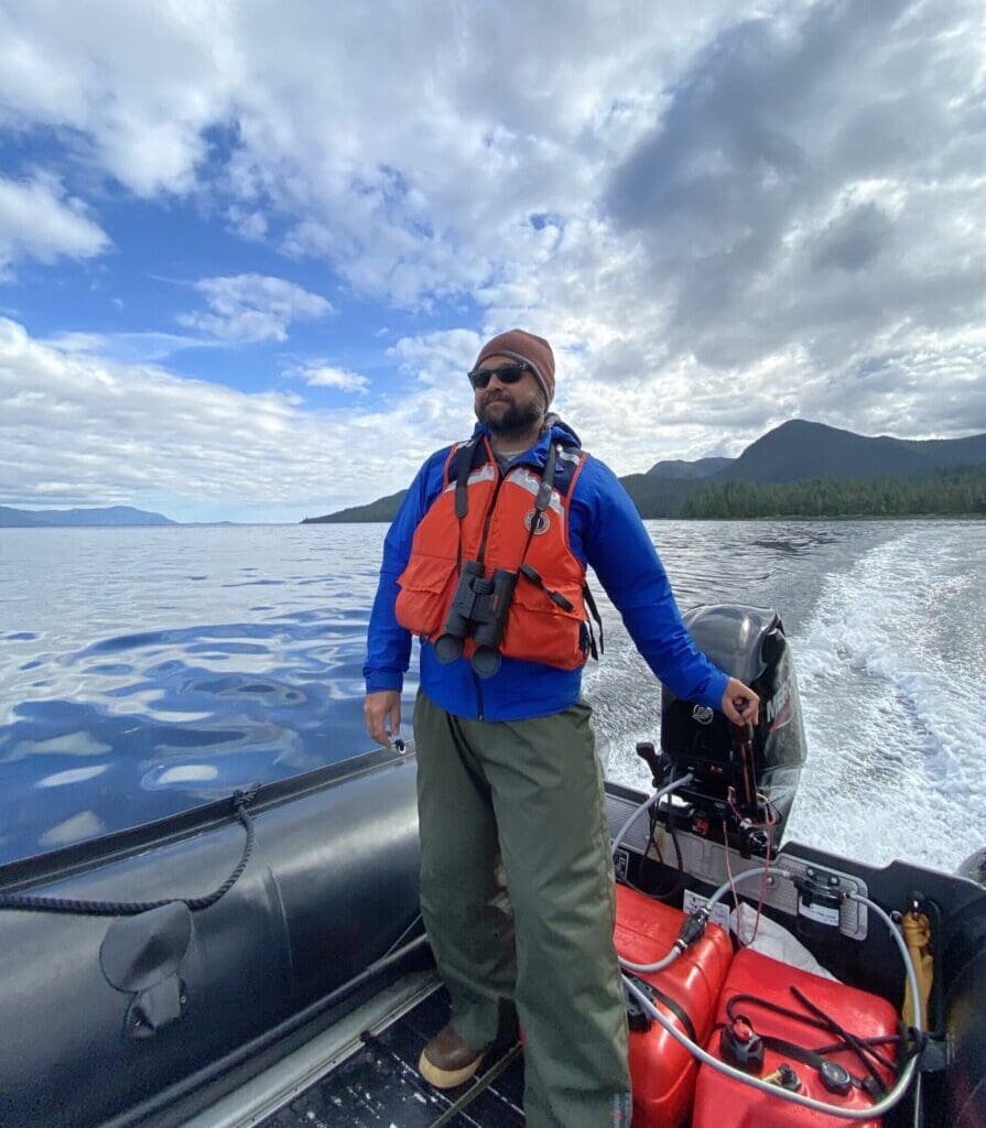 Man drives a Zodiac boat on a calm ocean under bright clouds and a patch of blue sky