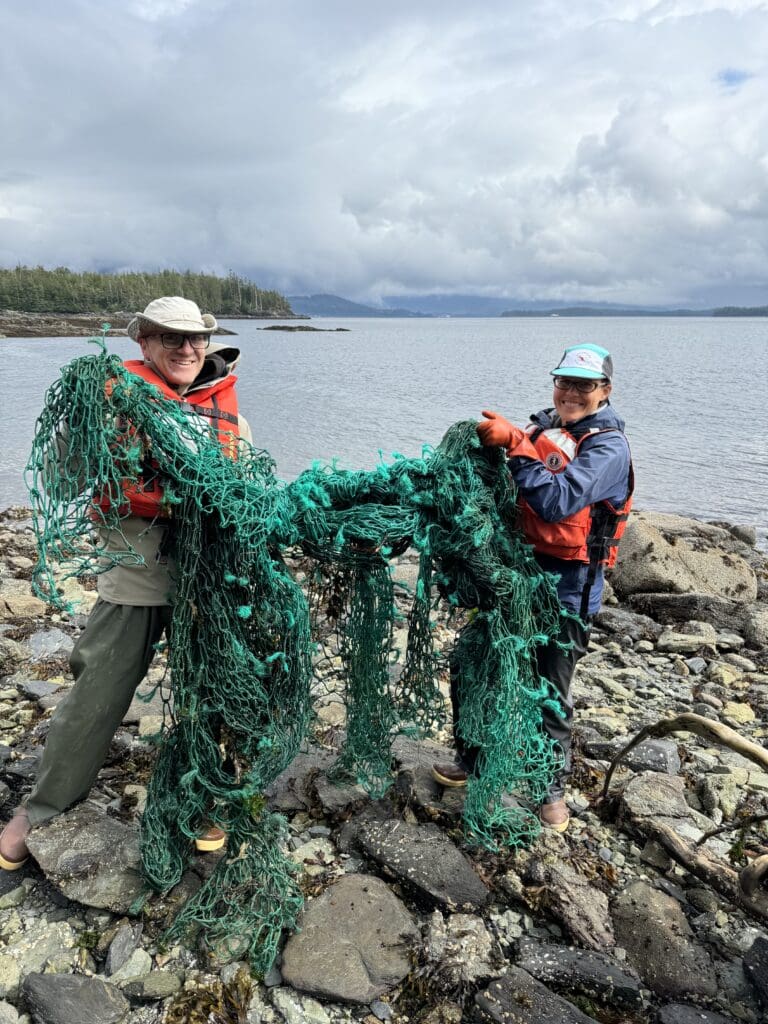 Two people holding a section of fishing net on a beach